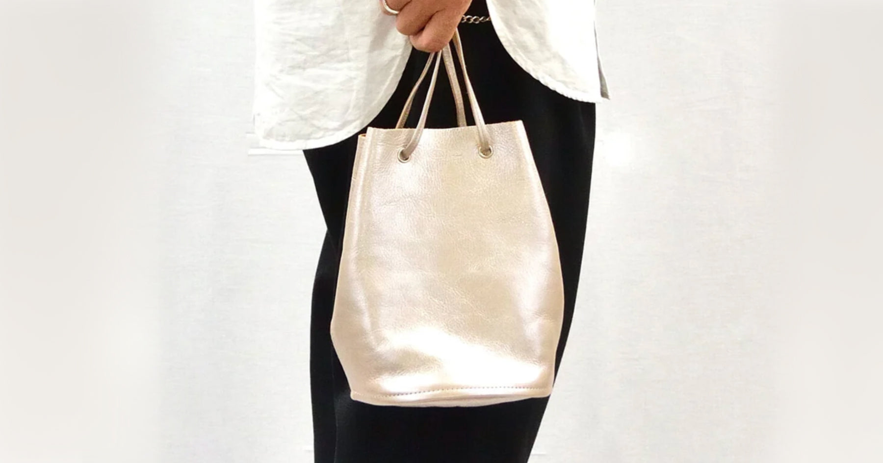 白いトップスに黒いズボンを履いた人が白の巾着バッグを持っている。